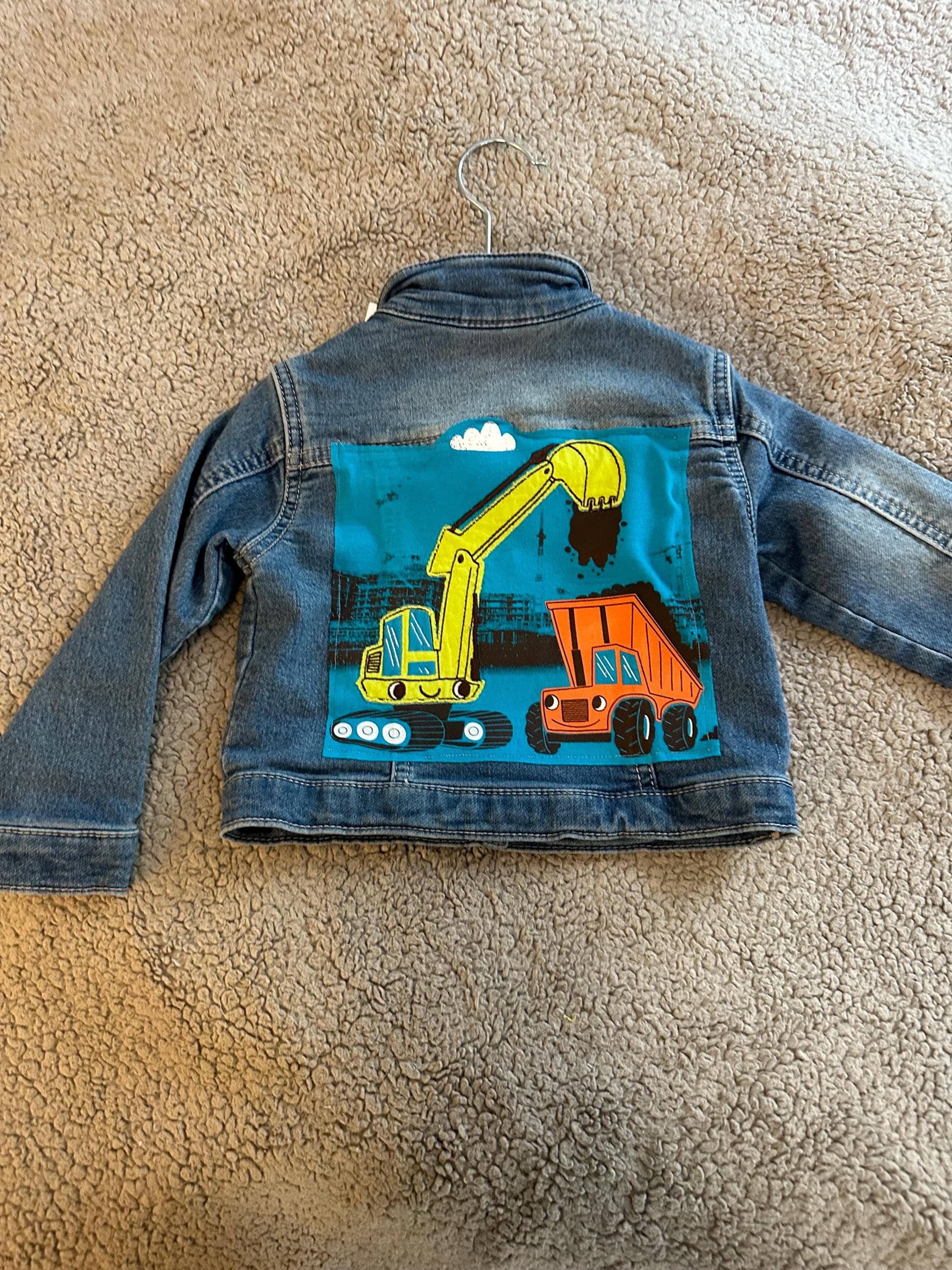 A loader and dump truck on back of denim jacket - Image 1