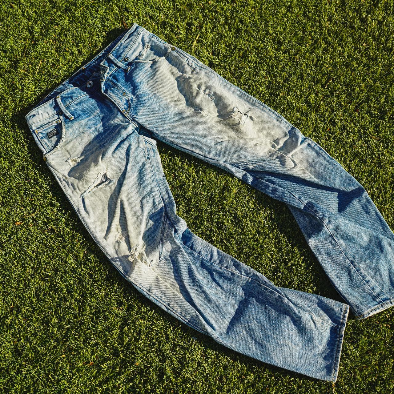 G-STAR Raw jeans in Men's Size 30. Features a light faded wash, with Japanese-style draped legs. Denim shows distress on the front, and back, and features G-STAR logo details throughout. - Thumbnail 3