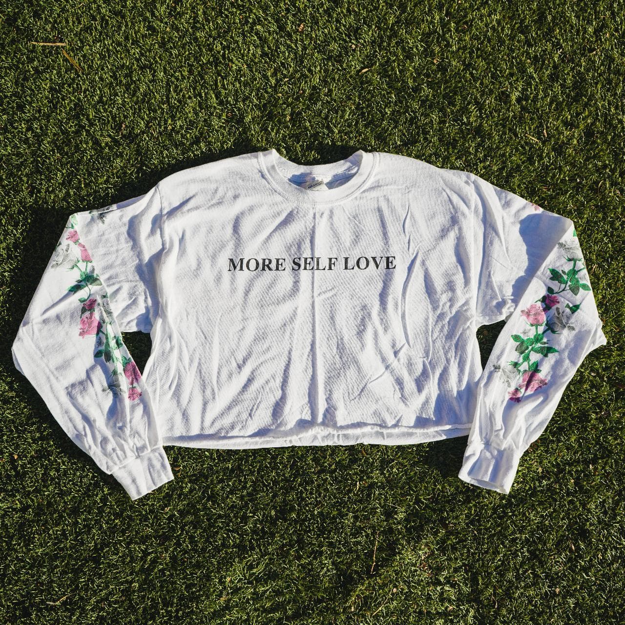 "More Self Love" long-sleeve cropped tee. Size women's medium. Features screen print text on the front and flowers on both sleeves. Seamless cropped bottom 🍉