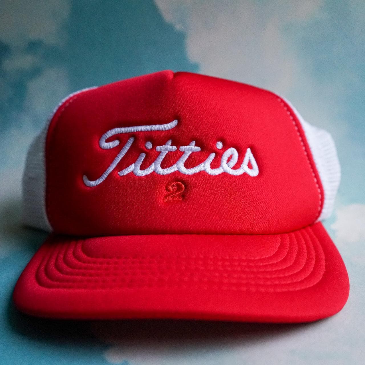 "Titties 2" trucker hat in red and white. Structured dome. Snap closure, red under brim, one size fits all.
