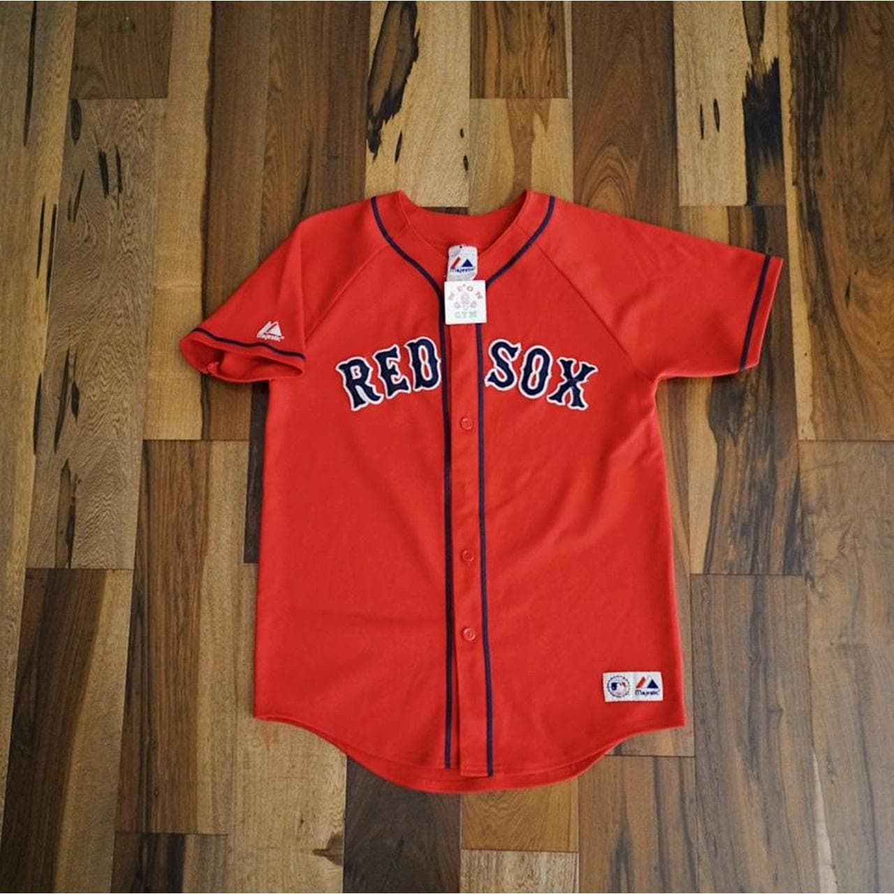 Majestic Boston’s Red Sox jersey in red with blue and white letters sewn on. Majestic logo accents throughout. No name on the back. Size M.