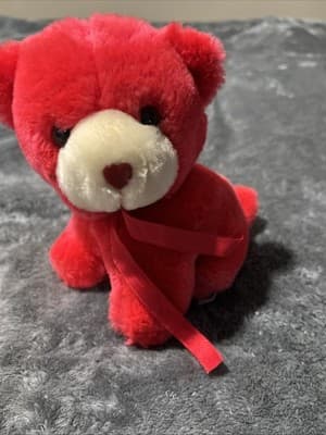 A vintage red plush teddy bear with a heart nose and ribbon.